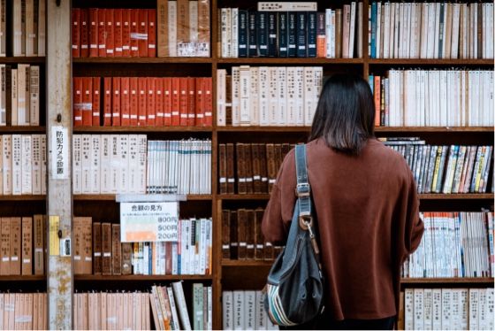 a woman stands in front of a bookshelf